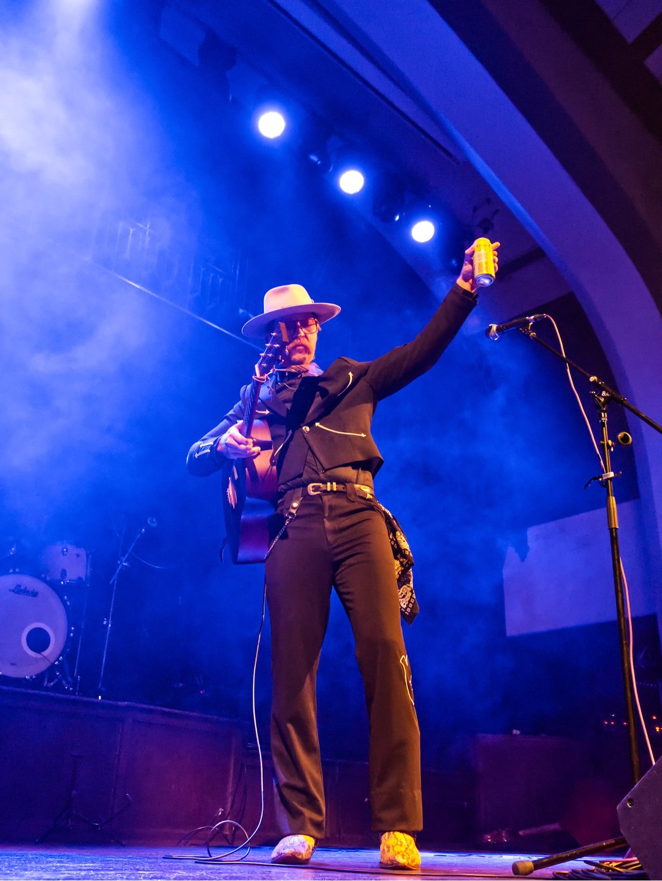 Trappers Pass on stage raising a can to the crowd under blue lights