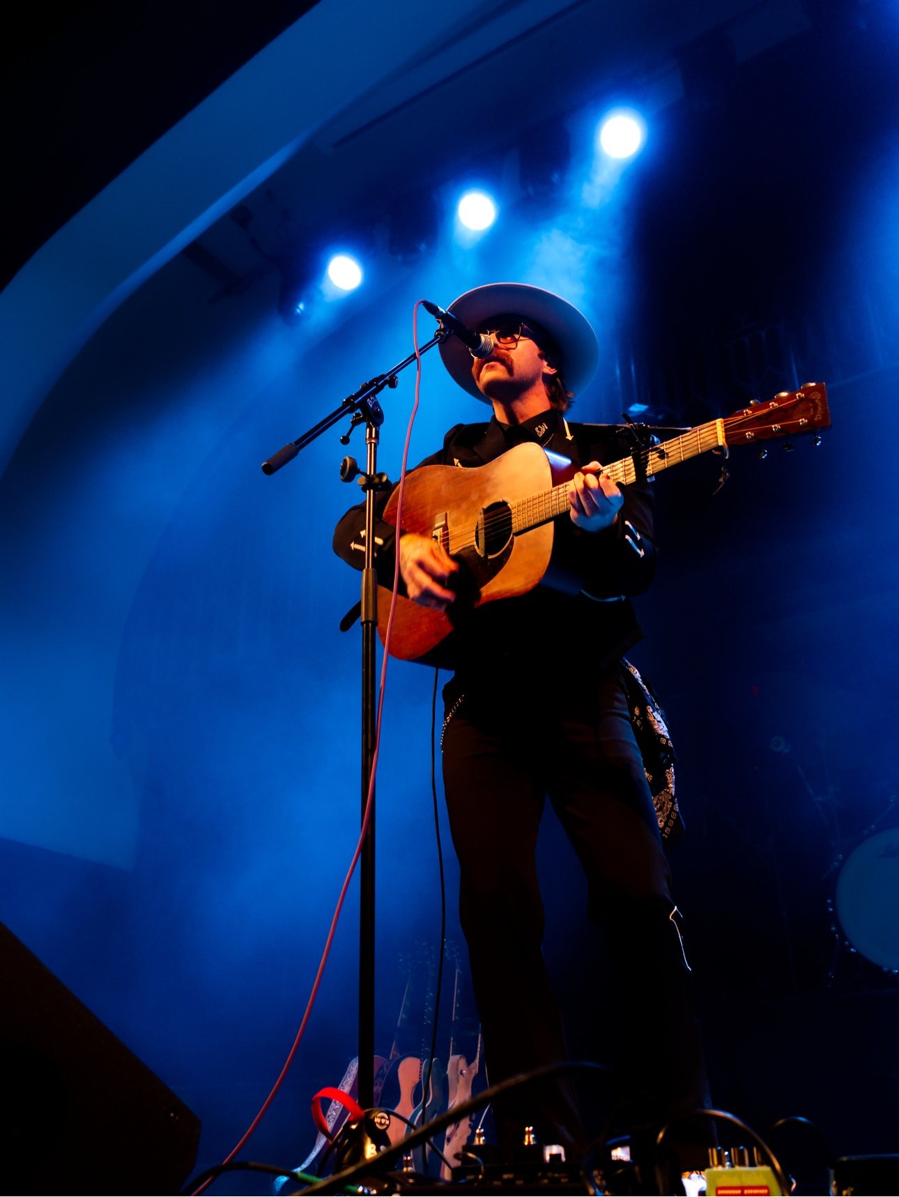 Trappers Pass playing acoustic guitar and singing under blue stage lights
